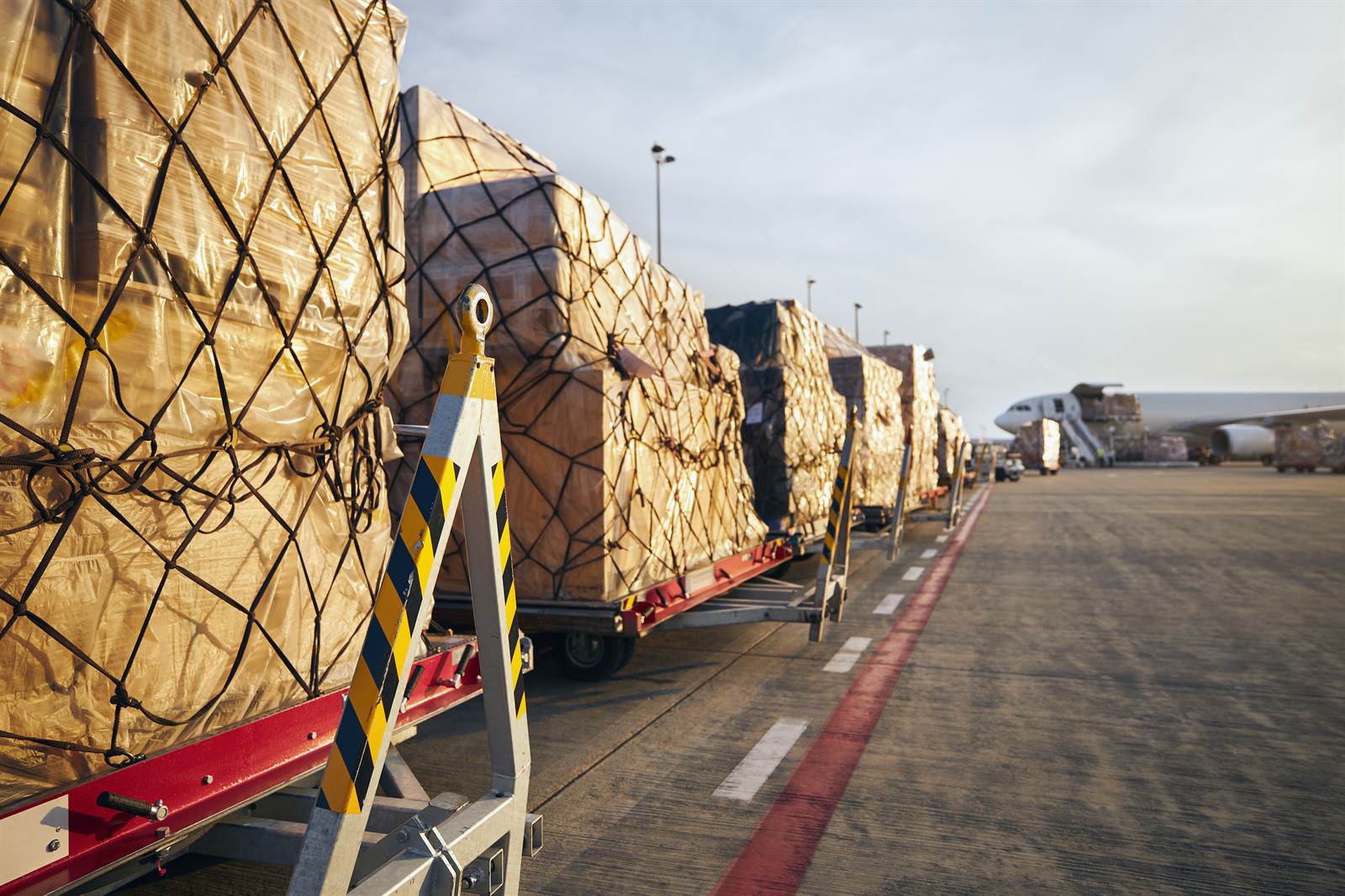 Netted air cargo pallets staged on the tarmac beside a freighter aircraft during loading