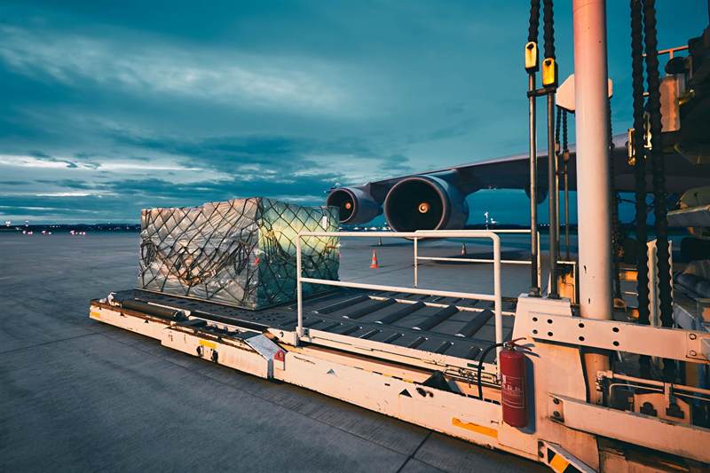 Netted air cargo pallet being loaded onto a freighter aircraft at dusk