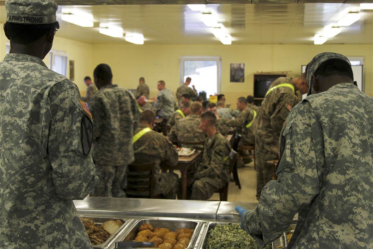 Service members dining at a military dining facility, seen from behind a stocked serving line